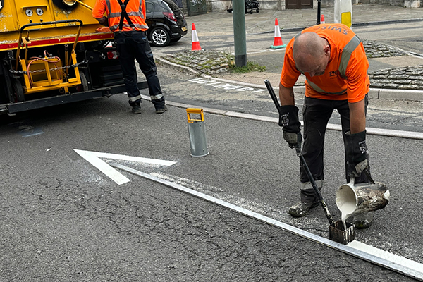 SWISCo team painting white arrow on road, using jug and roller