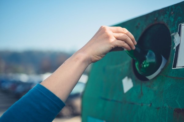 hand putting bottle into recycling bank