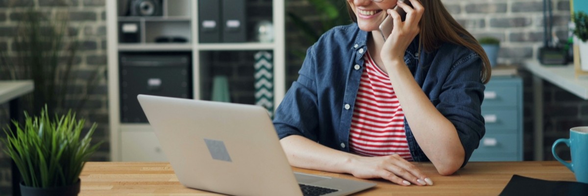 woman smiling whilst on phone and looking at laptop