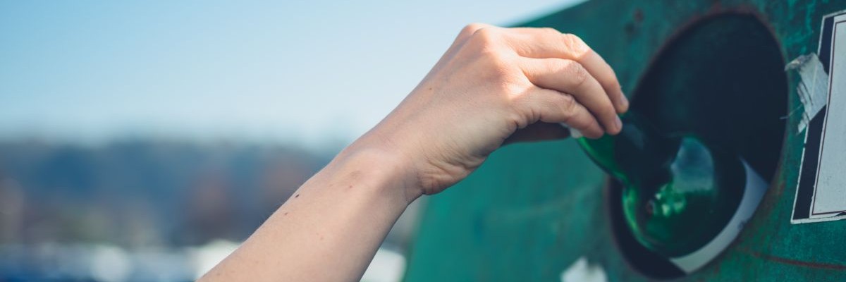 close up of hand placing bottle in recycling bank